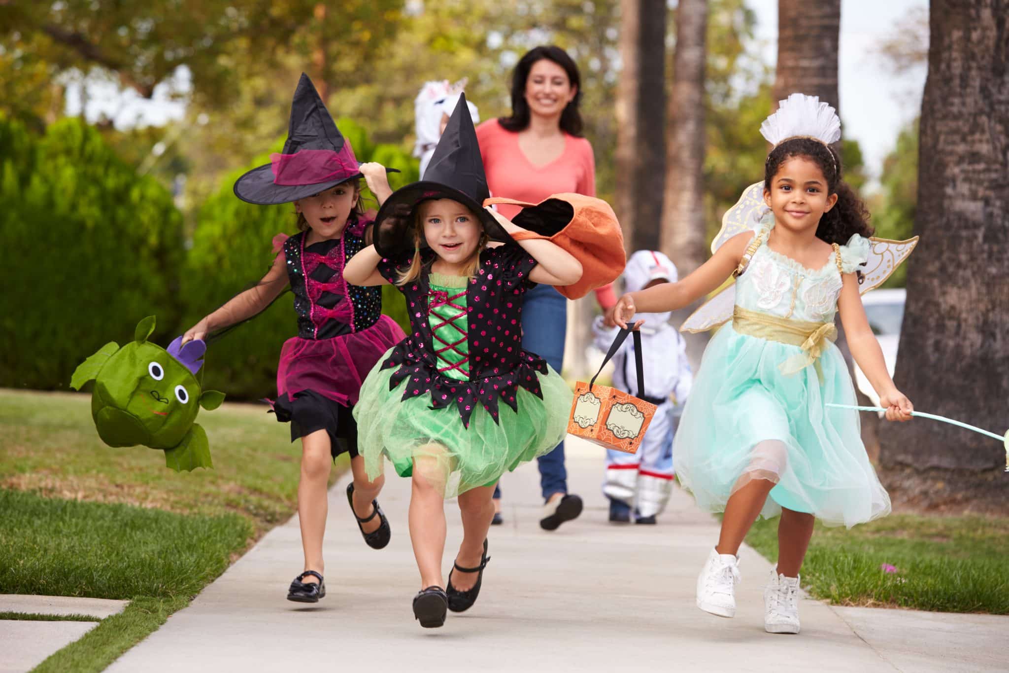 Children in costumes trick-or-treat with a parent close behind, illustrating safe, supervised Halloween outings.